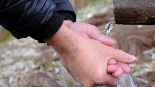 Male tourist washing his hands by spring water flowing from a tube in a park. Arms close-up.