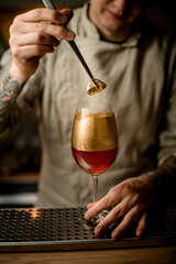 bartender holds golden piece of ice over glass with fizzy drink decorated with gold
