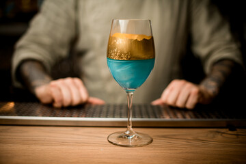 view on wine glass with blue drink decorated with gold standing on bar