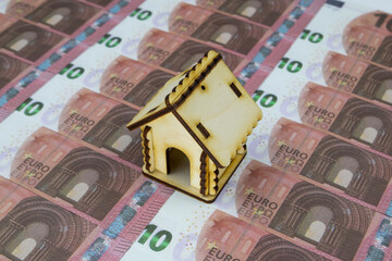 A small wooden house stands on 10 Euro banknotes lined up in a row