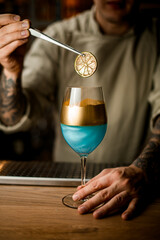 barman holds slice of citrus over wine glass decorated with gold