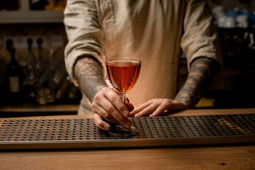 man bartender gently holds wine glass with alcoholic drink which stands on bar counter