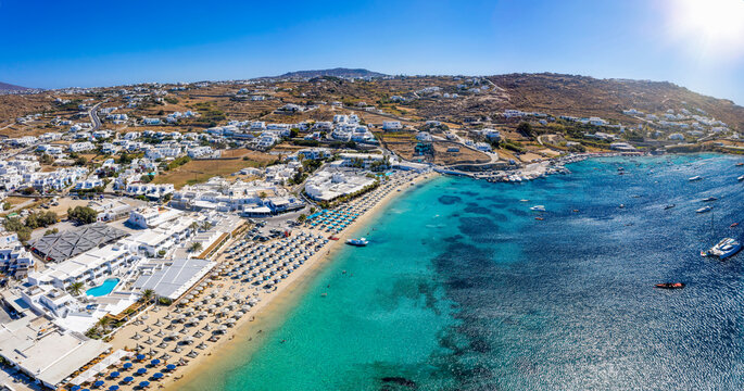 Panoramic aerial view to the popular beach of Ornos, Mykonos island, Greece, with turquoise sea and sun umbrellas lined up on the fine sand