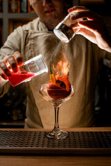 young man add ingredients to glass with vegetables inside and makes fire over it