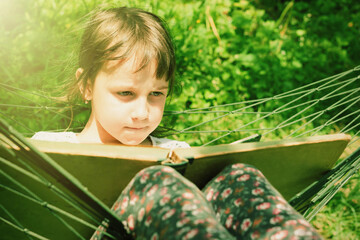 Learning always and everywher concept. Close up portrait of young beauutifuul girl reading book outdoors in hammock in park