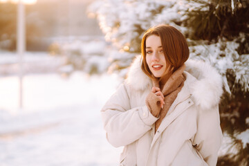 Beautiful woman in winter clothes posing in a snowy park. Young lady walking in a sunny winter day in the forest. Winter fashion, holidays, rest, travel concept.
