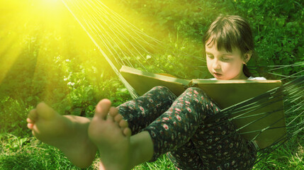 Young girl reading book in comfortable hammock against green grass. Pretty female child resting outdoors t green garden