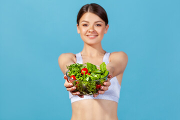 Slim positive woman holding in hands big bowl with vegetable salad looking at camera with smile,...