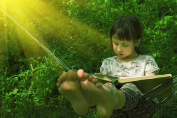 Portrait of young beautiful girl enjoying a book reading in  hammock outdoors at green garden in the rays of the sun. Selective focus on eyes