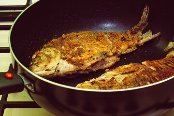 Fried crucian fish in breadcrumbs and onions in a frying pan. Golden crust of breadcrumbs. Freshwater fish.