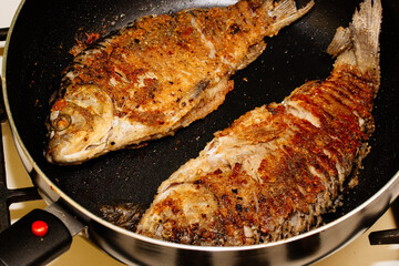 Fried crucian fish in breadcrumbs and onions in a frying pan. Golden crust of breadcrumbs. Freshwater fish.