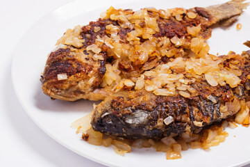 Fried crucian fish in breadcrumbs and onions in a plate on a white background. Golden crust of breadcrumbs. Freshwater fish.
