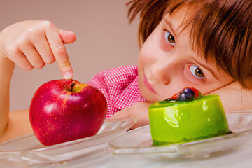 Close up portrait of beauiful young girl looking a red apple and green cake. She prefer fruit and vegetable Health, diet, lifestyle concept.