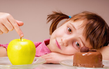 Young beautiful girl choosing between apple fruit and tasty cake.