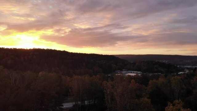 Sensational yellow pink clouds sunset, aerial drone rising above woods by road