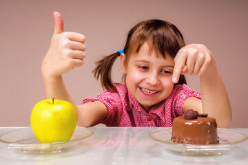 Portrait of young beautiful girl having hard choice between healthy and unhealthy food. She choosing between apple fruit and tasty cake.