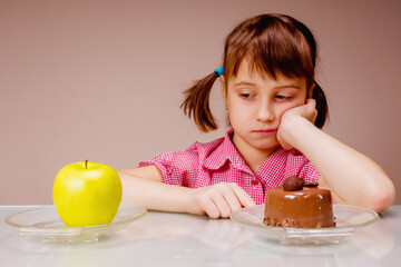 Portrait of young beautiful girl having hard choice between healthy and unhealthy food. She choosing between apple fruit and tasty cake. Health, diet, lifestyle concept. Selective focus on eyes.