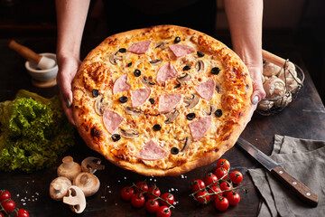 Capricciosa pizza with cheese, bacon and tomatoes and basil, on a dark background, top view