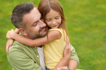 Obraz premium Portrait of happy young father and adorable little daughter hugging each other, standing with eyes closed while spending time in the green park on a summer day