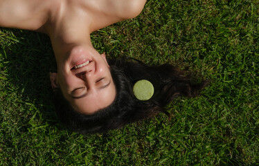 Young woman laying on the grass with natural eco friendly solid shampoo bar or conditioner on her...