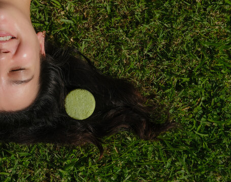 Young woman laying on the grass with natural eco friendly solid shampoo bar or conditioner on her hair. Zero waste and sustainable plastic free lifestyle