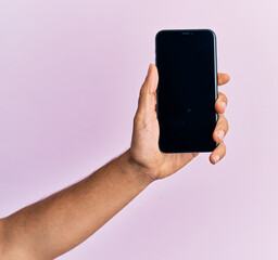 Hand of young hispanic man showing smartphone over isolated pink background.