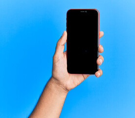 Hand of young hispanic man showing smartphone over isolated blue background.