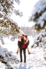 Young couple on winter holiday in a snowy forest. Happy man and woman having fun and laughing outdoors in winter. People, season, travel, love and leisure concept.