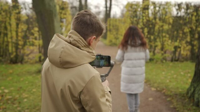 Mother with son walk in autumn park boy with mobile phone camera recording outdoor video blog. Teenager shooting video for travel vlogging. Catherine Park, Tsarskoye Selo, Saint Petersburg, Russia.