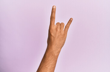 Arm and hand of caucasian young man over pink isolated background gesturing rock and roll symbol, showing obscene horns gesture