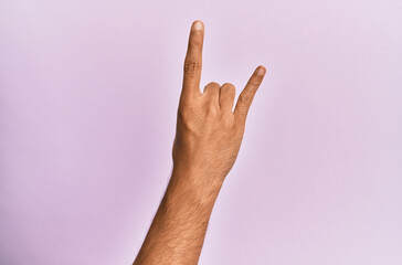 Arm and hand of caucasian young man over pink isolated background gesturing rock and roll symbol,...