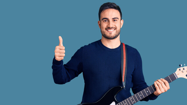 Young handsome man playing electric guitar smiling happy and positive, thumb up doing excellent and approval sign