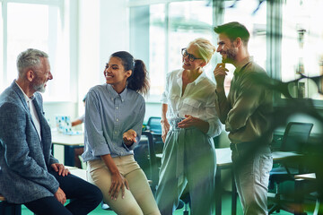 Group of cheerful business people communicating, discussing something and smiling while standing in the modern office or coworking space