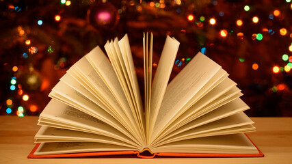 Warm, festive, happy atmosphere, christmas celebration, open children book on the table. Bright colorful lights of the holiday decoration on the background.