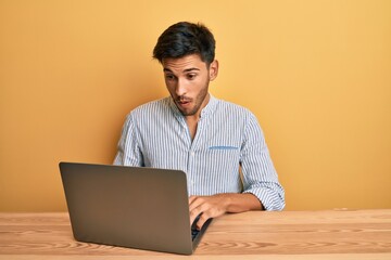 Young handsome man working at the office with laptop scared and amazed with open mouth for surprise, disbelief face