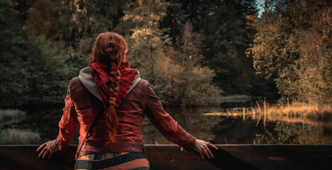 Single woman from behind with red hair looking at a lake in autumn