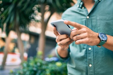 Young latin man using smartphone walking at the city.