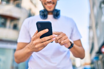 Young latin man smiling happy using smartphone and headphones at the city.