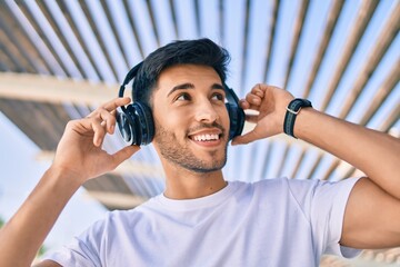 Young latin man smiling happy listening to music using headphones at the city.