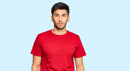Young handsome man wearing casual red tshirt relaxed with serious expression on face. simple and natural looking at the camera.
