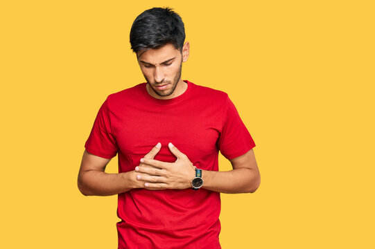 Young handsome man wearing casual red tshirt with hand on stomach because indigestion, painful illness feeling unwell. ache concept.