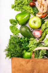 Green vegan food in full paper shopping bag, vegetables and fruits on white background. Shopping in supermarket, raw diet and clean eating concept. Healthy food