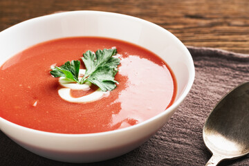 Bowl of tomato soup and spoon on wooden background