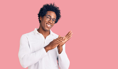 Handsome african american man with afro hair wearing casual clothes and glasses clapping and...