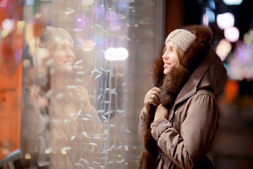 Obraz na płótnie Canvas happy girl lights evening christmas shopping standing on the street by the shop window