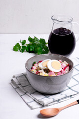 Russian cold soup Okroshka with vegetables, sausage, eggs and kvass in a bowl on the white table