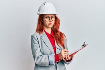 Young redhead woman wearing architect hardhat skeptic and nervous, frowning upset because of problem. negative person.