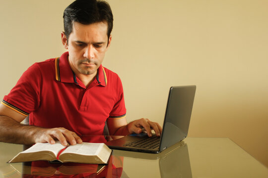 Adult man sitting at the desk in his living room with yellow background wall, reading the bible and writing notes on his notebook