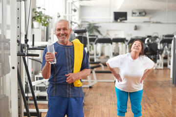Fototapeta na wymiar Happy senior man with bottle of water at gym. Smiling elderly man drinking water after gym session. Resting and refreshment.