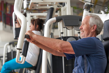 Senior man training at gym, side view. Elderly caucasian man training on machine at fitness club. Train your brain.